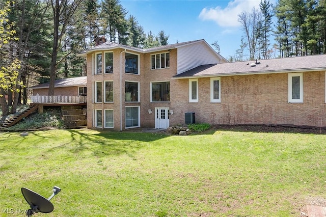 back of property with a chimney, stairs, central AC unit, brick siding, and a lawn
