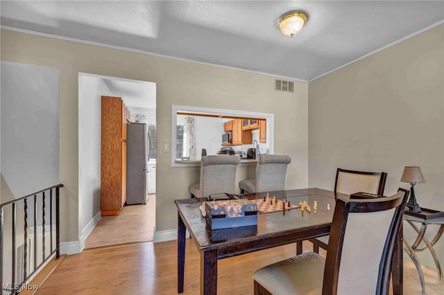 dining area featuring crown molding, baseboards, light wood-style flooring, and visible vents