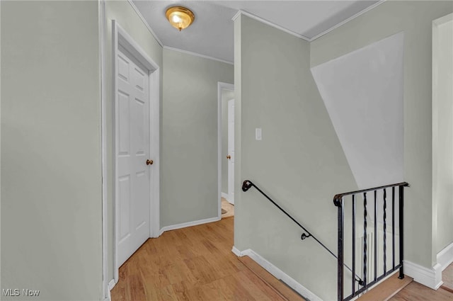 corridor featuring crown molding, light wood finished floors, baseboards, and an upstairs landing
