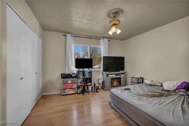 bedroom with baseboards, a glass covered fireplace, wood finished floors, and a closet