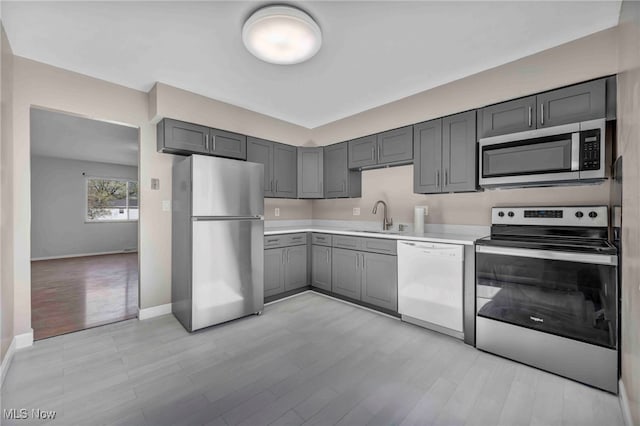 kitchen with a sink, baseboards, gray cabinets, and stainless steel appliances