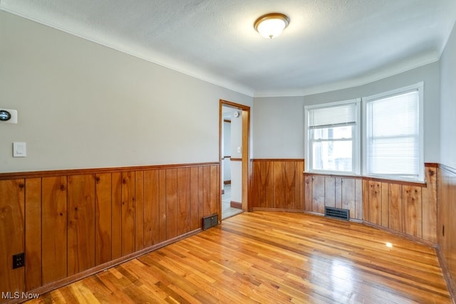 spare room with visible vents, light wood-style flooring, and a wainscoted wall
