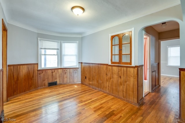 unfurnished room featuring visible vents, arched walkways, wood walls, wood finished floors, and a wainscoted wall