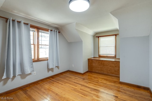 bonus room with baseboards, lofted ceiling, and light wood finished floors