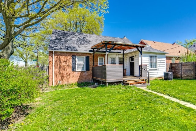 rear view of property with a lawn, central AC unit, brick siding, fence, and a shingled roof
