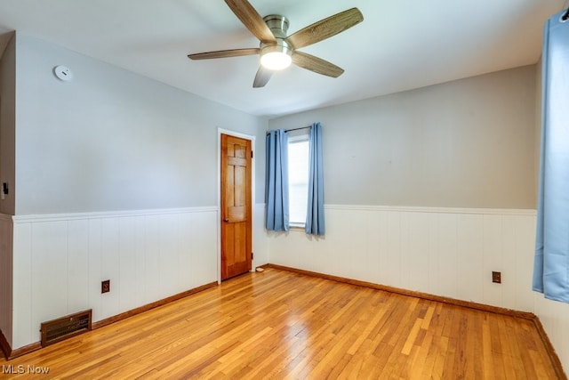 spare room with a ceiling fan, visible vents, wainscoting, and light wood-style floors