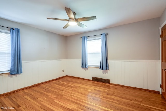 unfurnished room with visible vents, ceiling fan, wood finished floors, and a wainscoted wall