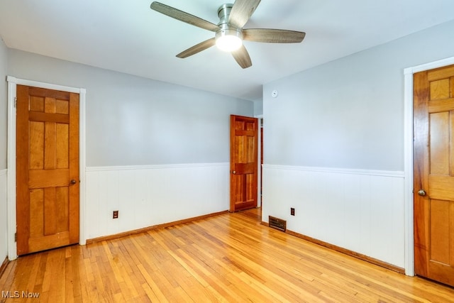 empty room featuring a ceiling fan, visible vents, wainscoting, and light wood-type flooring
