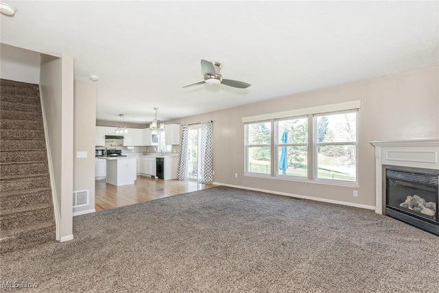 unfurnished living room with ceiling fan, visible vents, stairway, baseboards, and light carpet