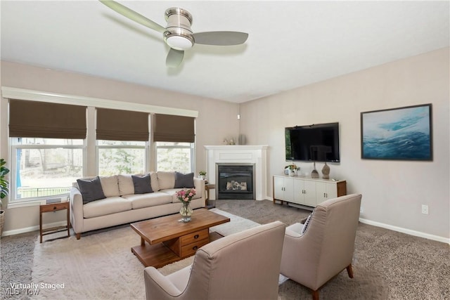 carpeted living area featuring a glass covered fireplace, baseboards, and a ceiling fan