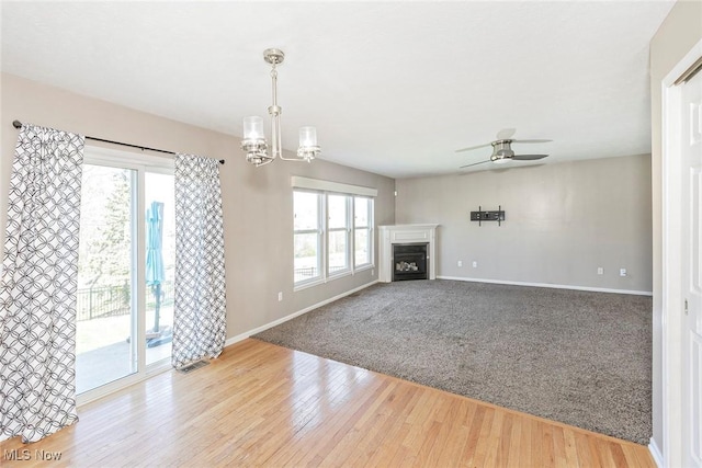 unfurnished living room featuring baseboards, a wealth of natural light, ceiling fan with notable chandelier, and a fireplace