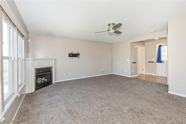 unfurnished living room with baseboards, carpet flooring, a glass covered fireplace, and a ceiling fan