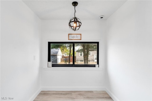 spare room featuring baseboards, light wood finished floors, and a notable chandelier