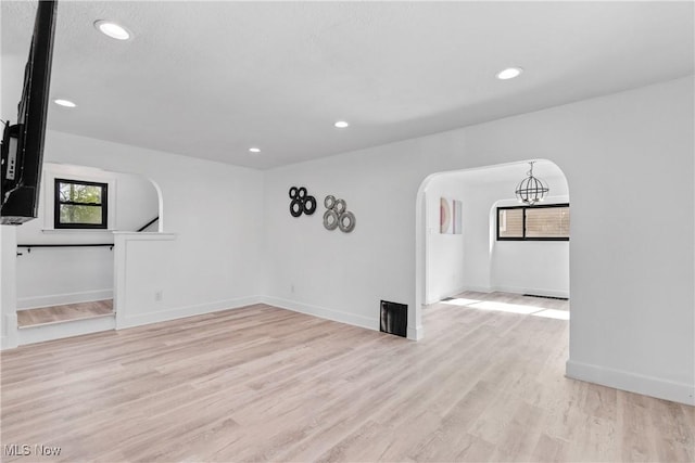 spare room featuring recessed lighting, arched walkways, light wood-style flooring, and baseboards