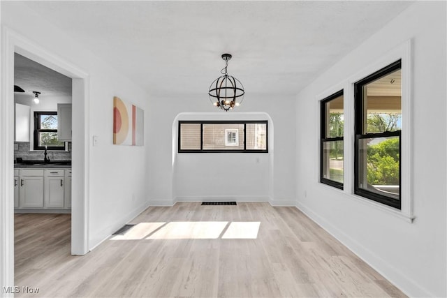 unfurnished dining area featuring an inviting chandelier, baseboards, plenty of natural light, and light wood-type flooring