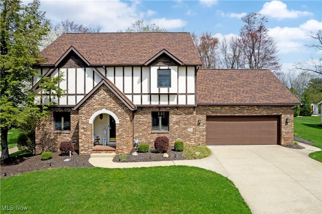 tudor-style house with brick siding, a shingled roof, a front yard, and concrete driveway