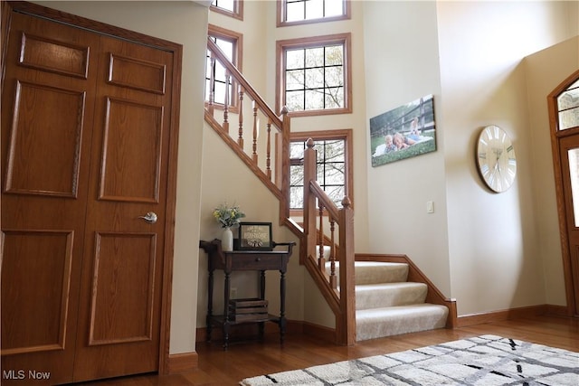 foyer with baseboards, wood finished floors, stairway, and a towering ceiling