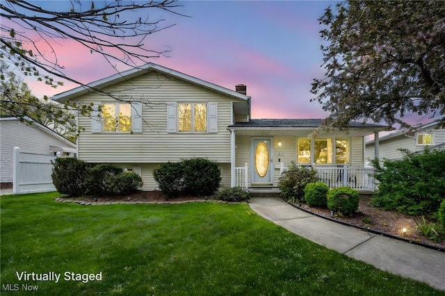 tri-level home with covered porch, a chimney, and a yard