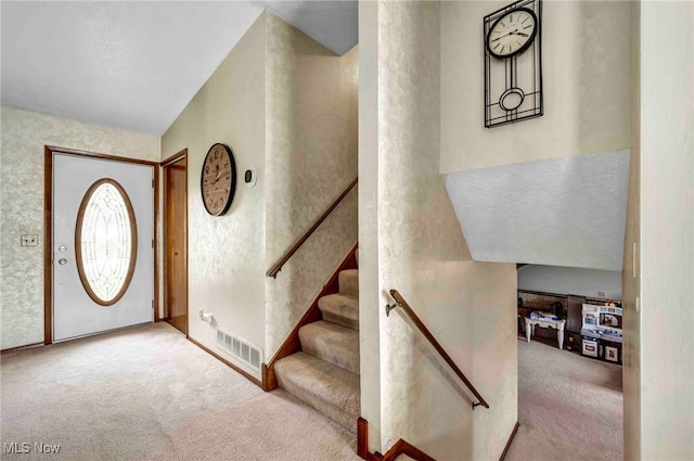 foyer with carpet floors, visible vents, stairs, a textured wall, and baseboards