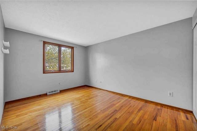 empty room with baseboards, visible vents, and wood finished floors