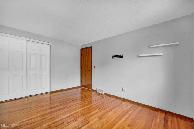 unfurnished bedroom featuring visible vents, a closet, baseboards, light wood-type flooring, and a textured ceiling