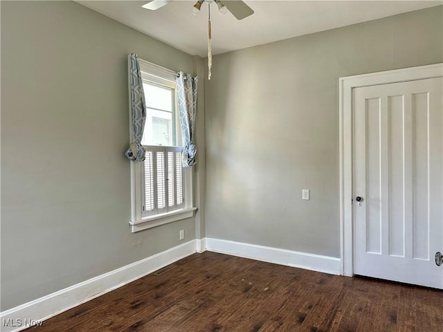 unfurnished room with baseboards, a ceiling fan, and dark wood-style flooring