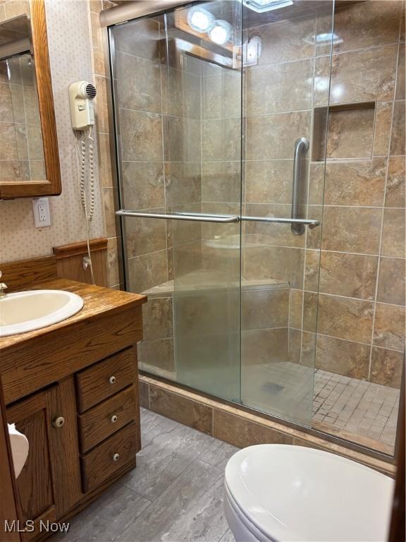 full bath featuring vanity, a stall shower, wallpapered walls, and toilet