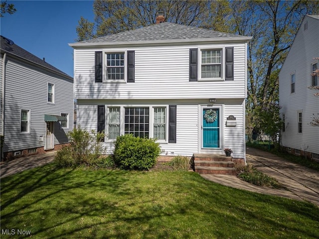 colonial inspired home featuring entry steps, a shingled roof, a chimney, and a front yard