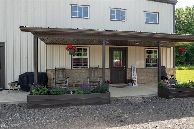 property entrance featuring covered porch, board and batten siding, metal roof, and stone siding