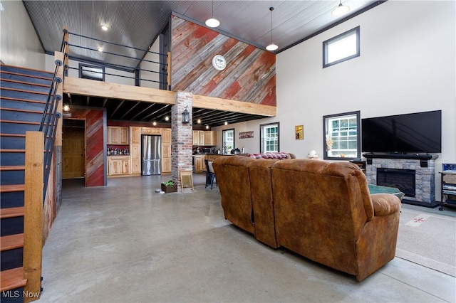 living area featuring a high ceiling, a stone fireplace, stairs, and finished concrete floors