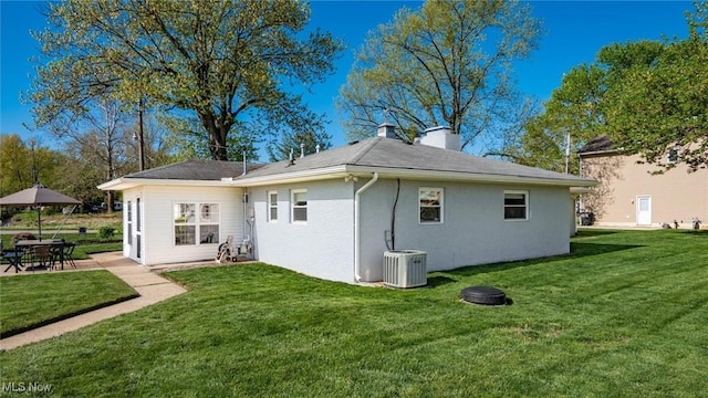 5130 Bateson Dr NE, Thornville, OH 43076 - rear view of house featuring central AC unit, stucco siding, a chimney, and a lawn