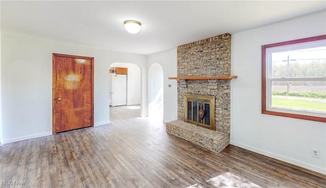 unfurnished living room featuring baseboards, arched walkways, wood finished floors, and a fireplace