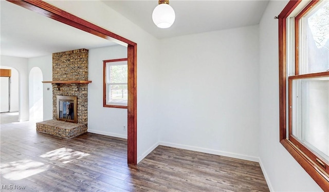 unfurnished living room featuring arched walkways, baseboards, a stone fireplace, and wood finished floors