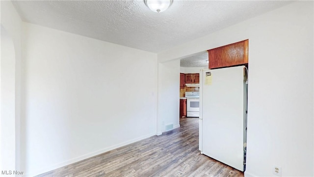 unfurnished room with baseboards, light wood finished floors, a textured ceiling, and visible vents