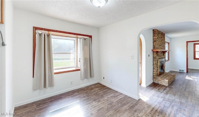 spare room featuring visible vents, arched walkways, a textured ceiling, and wood finished floors