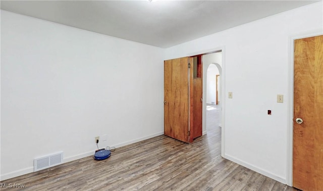 spare room featuring arched walkways, baseboards, visible vents, and wood finished floors