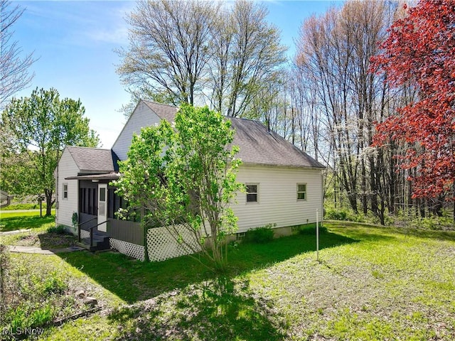 view of side of property featuring a sunroom, a lawn, and roof with shingles