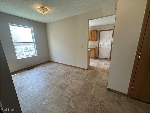 empty room with a textured ceiling, baseboards, and visible vents