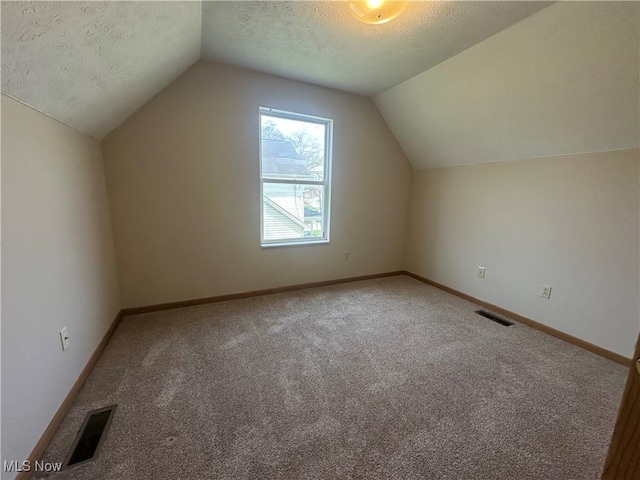 additional living space with carpet floors, lofted ceiling, a textured ceiling, and visible vents