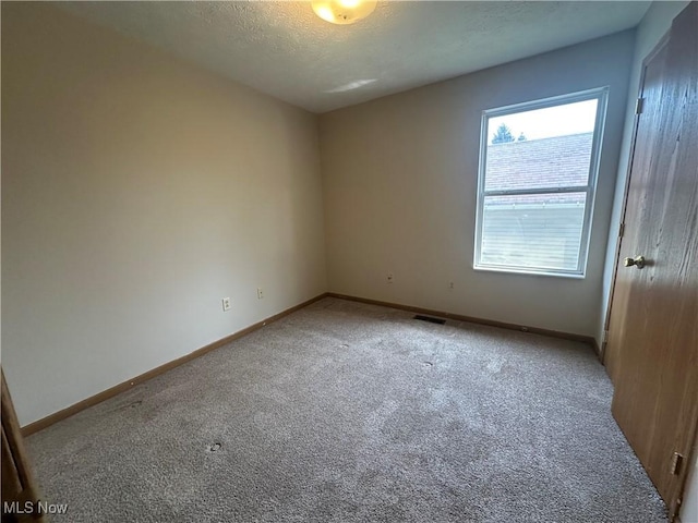spare room with baseboards, light carpet, a textured ceiling, and visible vents