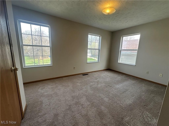carpeted spare room with a textured ceiling, visible vents, and baseboards