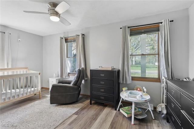 bedroom with baseboards, a nursery area, a ceiling fan, and wood finished floors