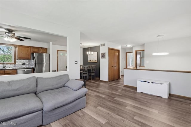 living area featuring radiator heating unit, visible vents, baseboards, ceiling fan with notable chandelier, and light wood-style floors