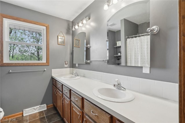 bathroom with a sink, baseboards, double vanity, and visible vents