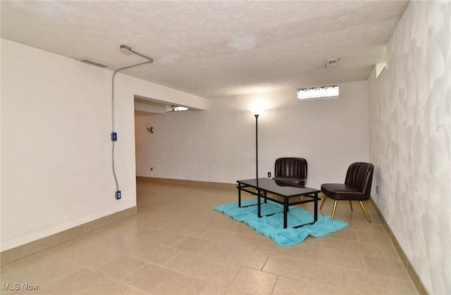 living area with baseboards, a textured ceiling, and visible vents