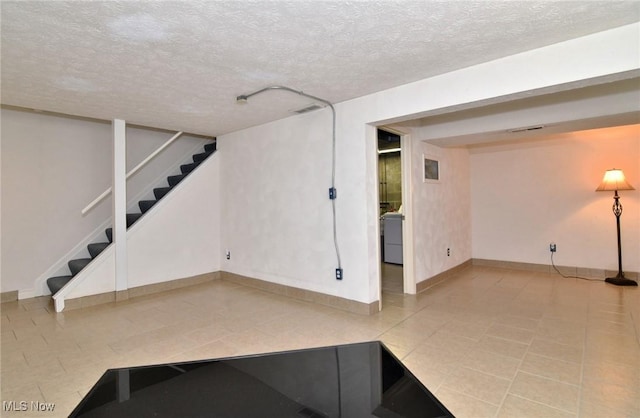 finished below grade area with a textured ceiling, stairs, and washer / dryer