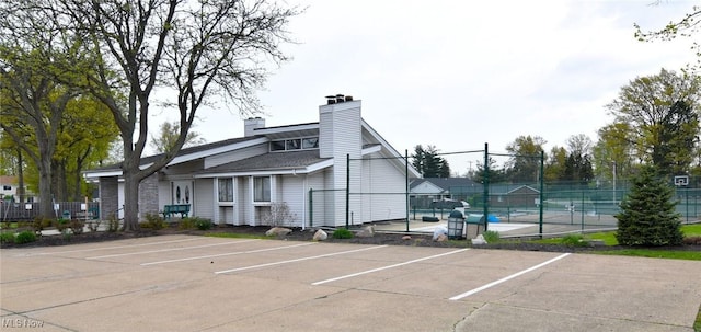 uncovered parking lot featuring a tennis court and fence