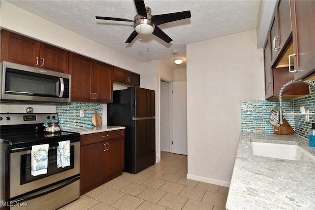 kitchen with appliances with stainless steel finishes, a textured ceiling, a ceiling fan, light tile patterned floors, and backsplash