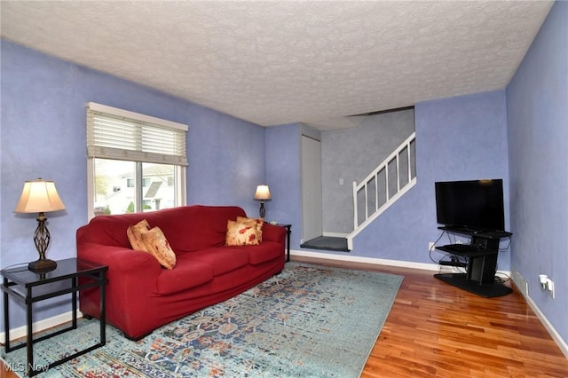 living room with baseboards, a textured ceiling, wood finished floors, and stairway