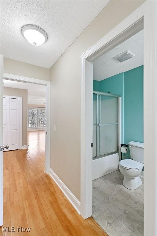 hallway with baseboards, light wood-style flooring, a textured ceiling, and visible vents
